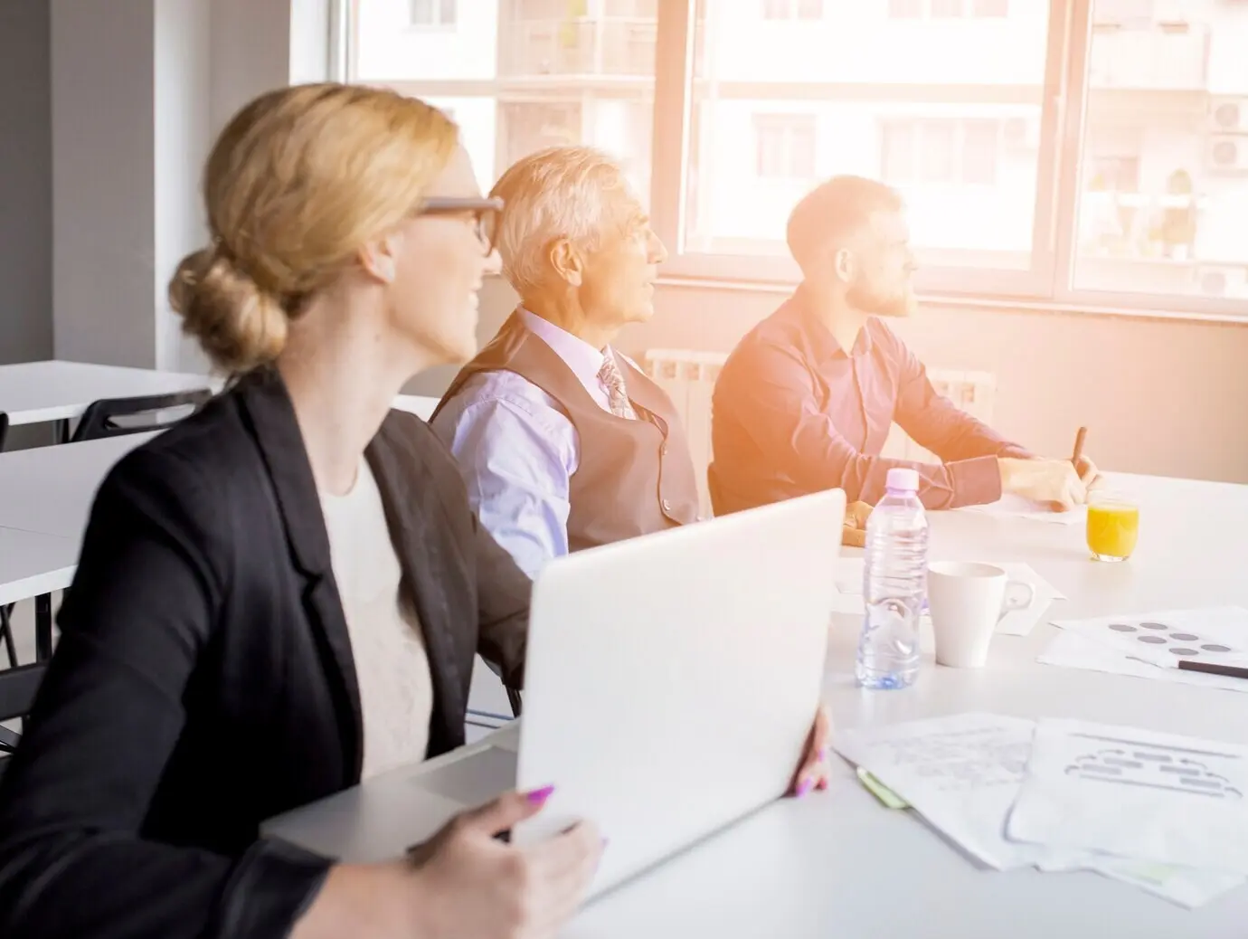 A young businesswoman with a laptop sits with colleagues in the meeting.
